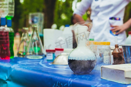 桌上摆着各种各样的化学器皿。前面是一个烧瓶，里面有化学反应。科学化学实验