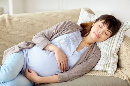 怀孕、休息、人和期望概念-睡觉在沙发的愉快的孕妇在家。睡觉在沙发上的愉快的孕妇在家