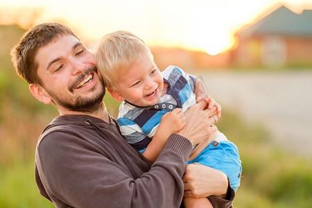 快乐的男人和他的孩子在户外玩耍。家庭生活方式，夕阳下父子俩的田园风光。