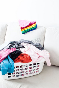 叠衣服摄影照片_在篮子里洗衣服，在沙发上放一叠干净的亚麻布。五颜六色的干净衣服