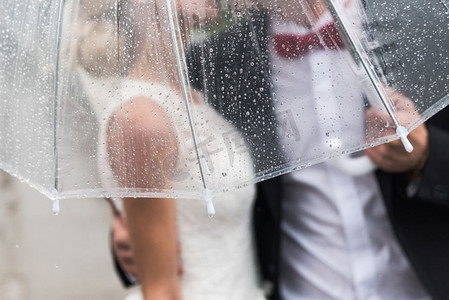 新郎新娘在雨中打着一把透明的雨伞，雨点