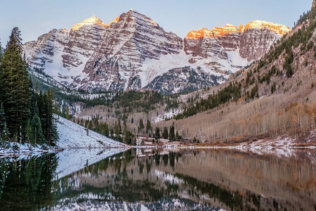 美国科罗拉多州秋天的黎明时分，栗色的钟声和栗色的湖水在雪地里倒映着岩石和山脉。