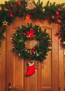 圣诞花环摄影照片_门上有红色袜子和花边的圣诞花环。门上挂着圣诞花环