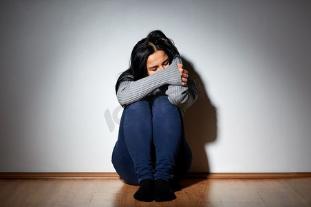 人，悲痛和家庭暴力概念-不愉快的妇女坐在地板和哭在家里。不幸的女人在家里的地板上哭泣