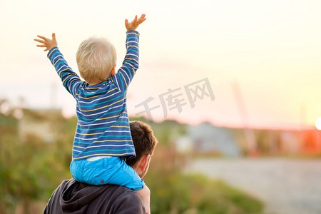 快乐的男人和他的孩子在户外玩耍。家庭生活方式，夕阳下父子俩的田园风光。