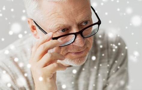 老年、问题和人的观念--戴眼镜的老人在雪中思考的特写。戴眼镜的老人思考特写