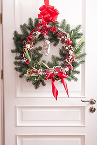 白色的门上挂着圣诞花环。红白元素，为装饰度假屋鞠躬。红白相间的圣诞花环