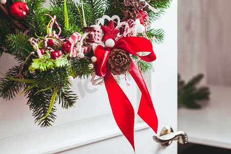 白色的门上挂着圣诞花环。红色和白色的元素，蝴蝶结装饰度假屋。红色和白色的圣诞花环