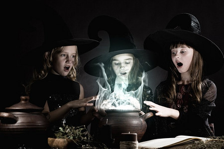 万圣节恶魔摄影照片_小女巫。三个万圣节小巫婆在锅上念咒语