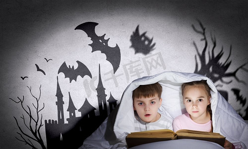 孩子们的噩梦。两个小孩子在毯子下看书