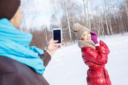 在冬季公园散步。冬日公园里的一位年轻男子在为他的女朋友拍照