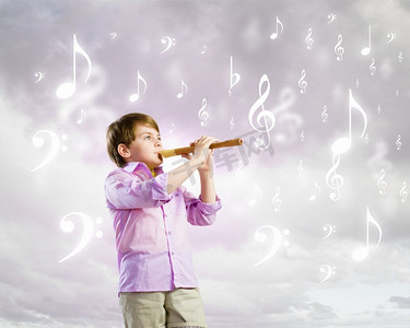 风吹儿童摄影照片_吹长笛的男孩。多云背景下吹长笛的小男孩形象