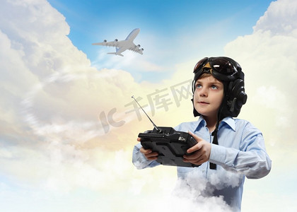 戴着飞行员头盔的小男孩在云的背景下玩玩具无线电飞机