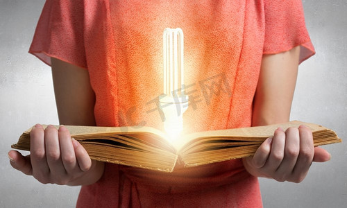 阅读可以开阔你的视野。近距离看妇女拿着书页上有灯泡的书