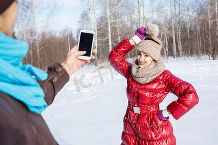 他在散步摄影照片_在冬季公园散步。冬日公园里的一位年轻男子在为他的女朋友拍照