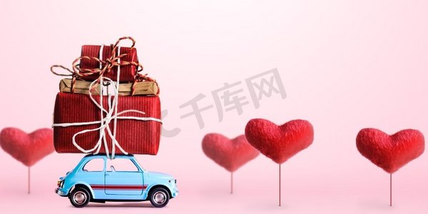 问候摄影照片_蓝色复古玩具车送情人节礼盒，粉色背景，心形树