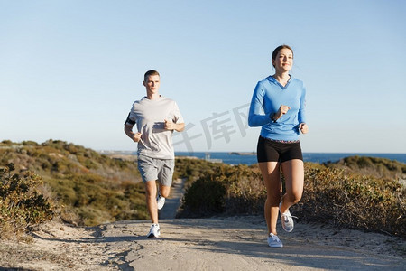 运动跑步者在海滩上慢跑，和她的伴侣一起锻炼。健康的女健身模特和她的伴侣沿着海洋慢跑