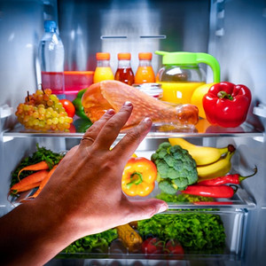 冰箱水果摄影照片_夜间，在敞开的冰箱里，人们伸手去拿火鸡腿食物