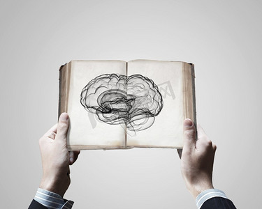心智能力。男性手持翻开的带有大脑图片的书的特写
