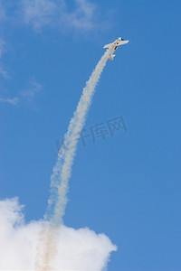 一架尾随烟雾的特技飞机以平滑的弧线向上飞向明亮的蓝天。