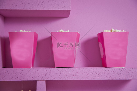 街拍背景图片_爆米花从条纹盒子溢出。三个复古风格的爆米花盒在嘉年华主题静物与街机游戏粉红色门票。一个宽大的经典盒剧院爆米花隔离在粉红色 .
