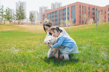 妈妈和女儿在草坪上与一只比熊玩耍