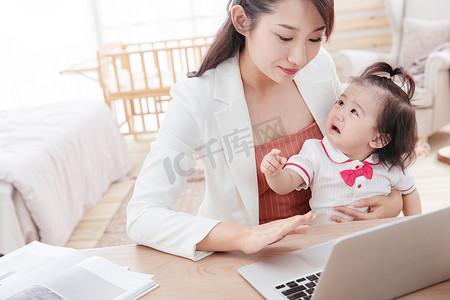 伤心妈妈摄影照片_年轻妈妈抱着孩子使用电脑