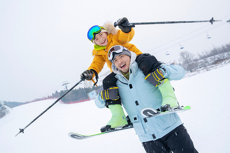 滑雪场上拿滑雪杖的快乐男孩骑在父亲脖子上