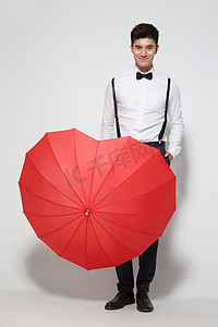 彩色爱心背景摄影照片_青年男人拿着心形红雨伞
