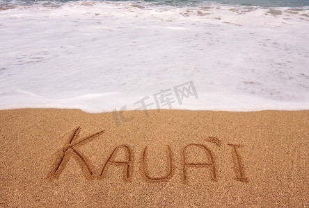 飞溅沙子摄影照片_汹涌的潮水前写在沙子上的考艾岛这个词