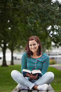 微笑的休闲学生坐在长椅上阅读