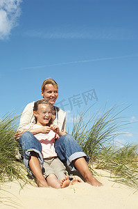 快乐的妈妈和小女儿坐在沙滩上的沙滩上