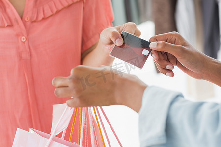 顾客从女售货员那里收到购物袋和信用卡的中间部分
