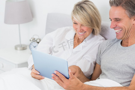 笑着在床上使用 tablet pc 的夫妇