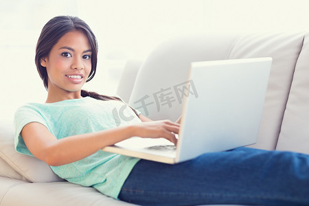 原创大气首页摄影照片_躺在沙发上的漂亮女孩用她的笔记本电脑对着相机微笑