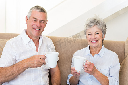 坐在沙发上喝咖啡的老夫妇对着镜头微笑