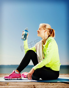 健身运动女摄影照片_妇女在户外运动后喝水
