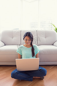 年轻的微笑女孩坐在地板上，用她的笔记本电脑
