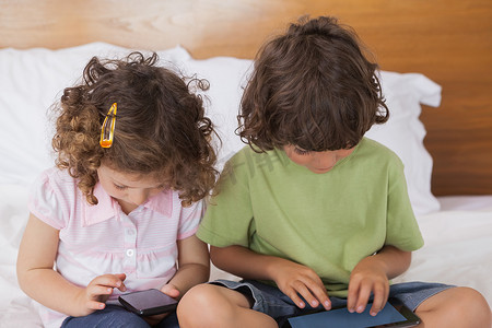 孩子们在床上使用数字平板电脑和手机