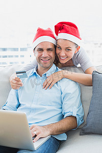 戴着圣诞帽的幸福夫妻用笔记本电脑在网上购物