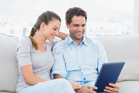 微笑的夫妇坐在沙发上使用 tablet pc