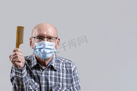 戴眼镜的老头摄影照片_秃头老头戴着眼镜，戴着医用面具，手里拿着梳子。