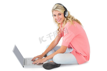 漂亮的年轻金发女郎坐着用笔记本电脑听音乐