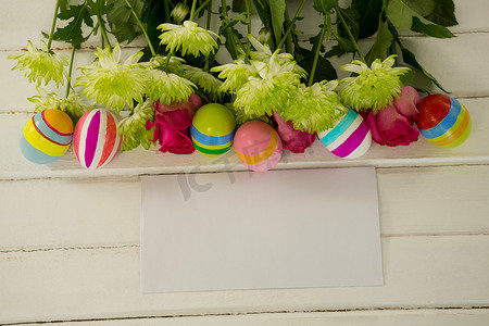 彩绘装饰摄影照片_木制背景上彩绘的复活节彩蛋、一束花和信封