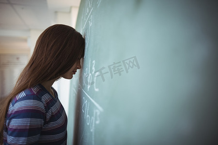 疲惫的女学生闭着眼睛站在教室的黑板附近