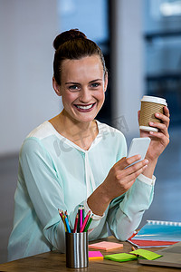 职业女人摄影照片_在手机上拿着咖啡杯和短信的女人