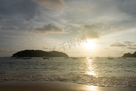 日落天空的景色和漂浮的小船和海滩上的小岛的轮廓