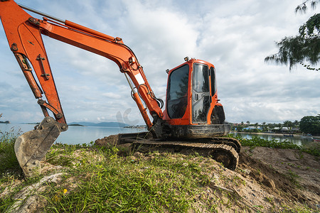 在蓝天和大海的映衬下，地面上的小型橙色挖掘机用于建筑工地的工程。