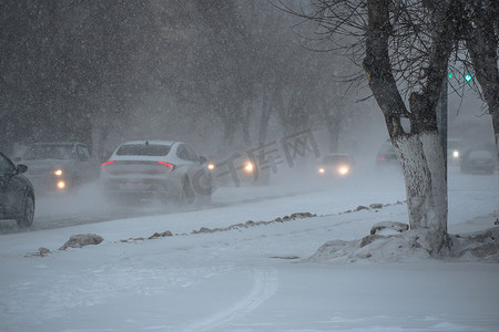 冬天，在暴风雪、暴风雪或降雪中，城市的恶劣天气下，积雪覆盖的道路上有汽车。北方的极端冬季天气条件。汽车驶过城市积雪覆盖的街道