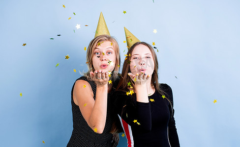 两个戴着生日帽的年轻女性拿着气球在蓝色背景下庆祝生日